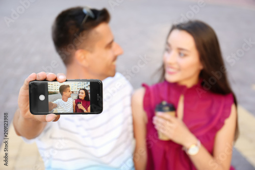 Young couple taking selfie outdoors, focus on smartphone