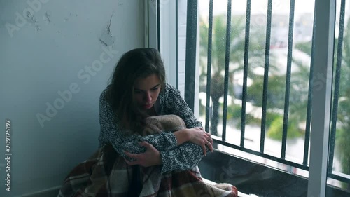 Depressed woman sitting on the floor by the window with the rain falling outside. Lonely woman in despair with the suicide thoughts.
