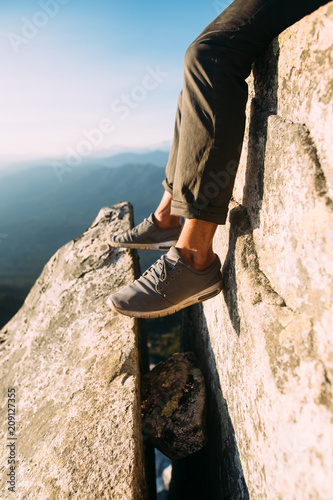 Man In Tennis Shoes Hanging Legs Over Edge of Rock photo