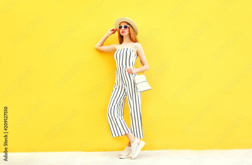 Fashion woman is posing in white striped pants, round hat on colorful yellow background Fashion woman is posing in white striped pants, round hat on colorful yellow background