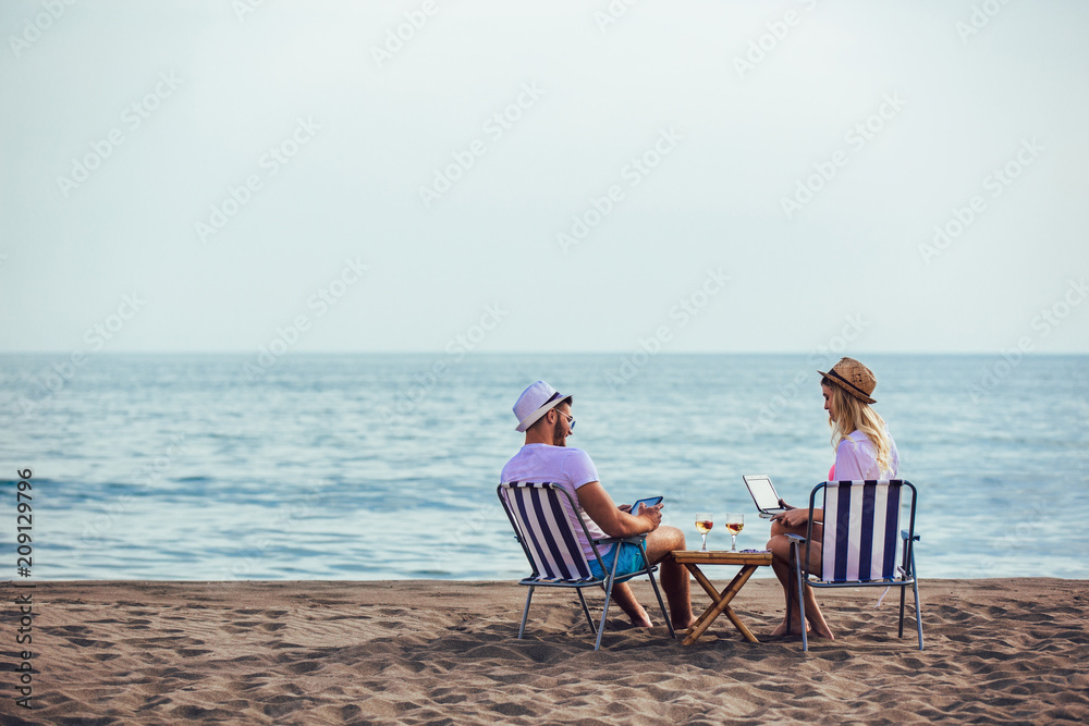 Happy smiling couple surfing the net and enjoy the summer at tropical beach using laptop and digital tablet