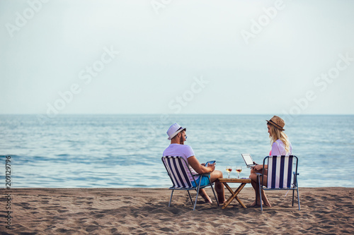 Happy smiling couple surfing the net and enjoy the summer at tropical beach using laptop and digital tablet © Mediteraneo