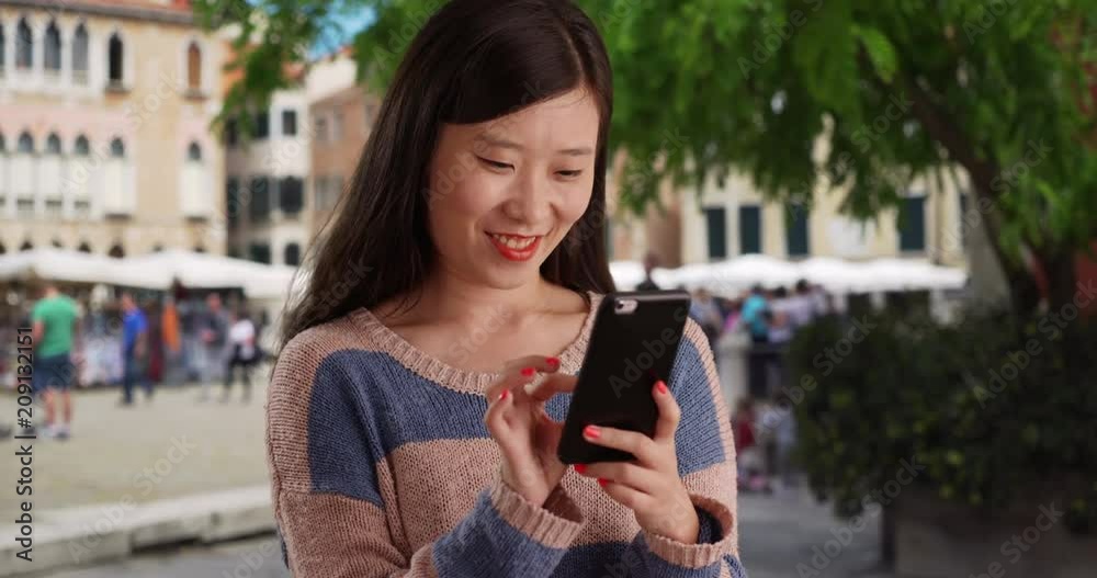 Hip young pretty lady using smartphone and reading text messages in Venice Italy, Close up of lovely Asian female millennial sending texts with cell phone in old European city, 4k