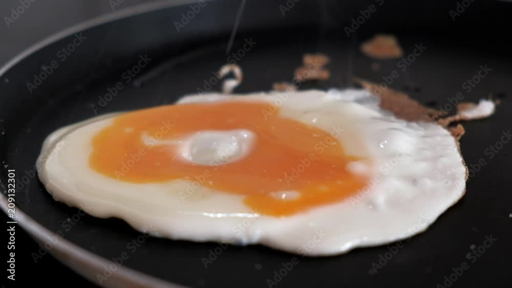 Close-up of salting one egg being fried on a frying pan. Yolk spread on the protein. Scrambled eggs cooking. 4k video. Close-up of salting one egg being fried on a frying pan. Yolk spread on the protein. Scrambled eggs cooking. 4k video.