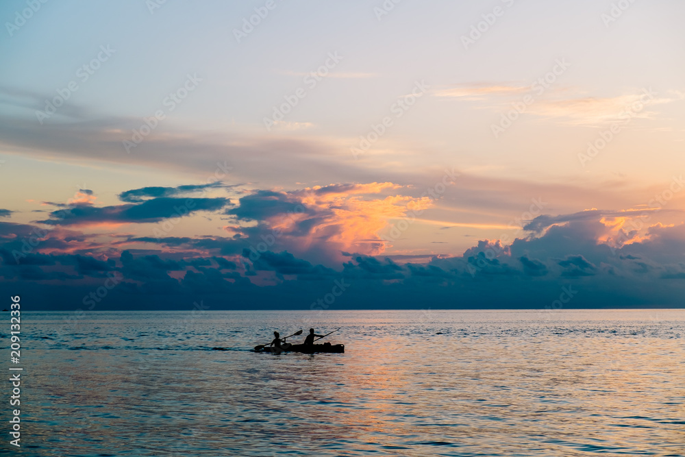 a young couple is kayaking in the Indian ocean, Maldives. Beautiful sunset in the background