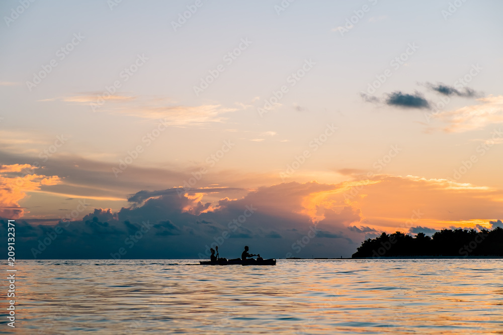 a young couple is kayaking in the Indian ocean, Maldives. Beautiful sunset in the background