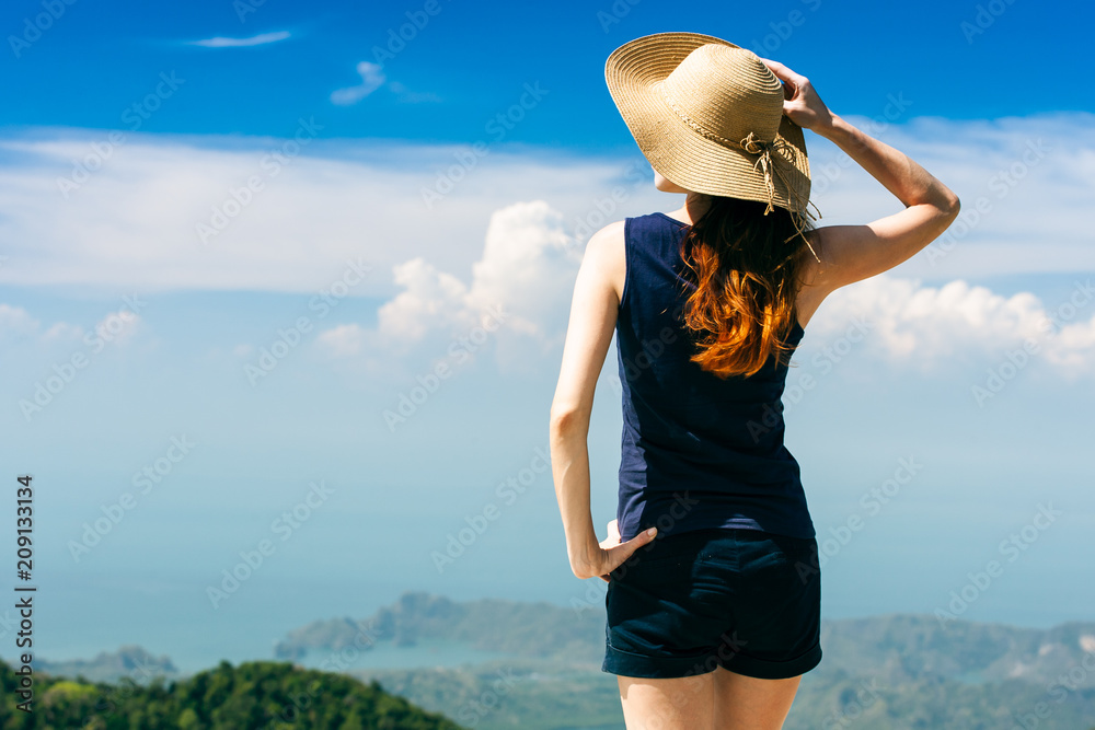 Young traveling woman wearing hat and standing on the top of the mountain cliff