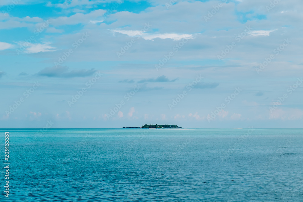 Maldives background. Sunset over the tropical sea and coral beach with colorful clouds in the sky. Boats on the horizon in heavenly atoll of peace and relaxation.