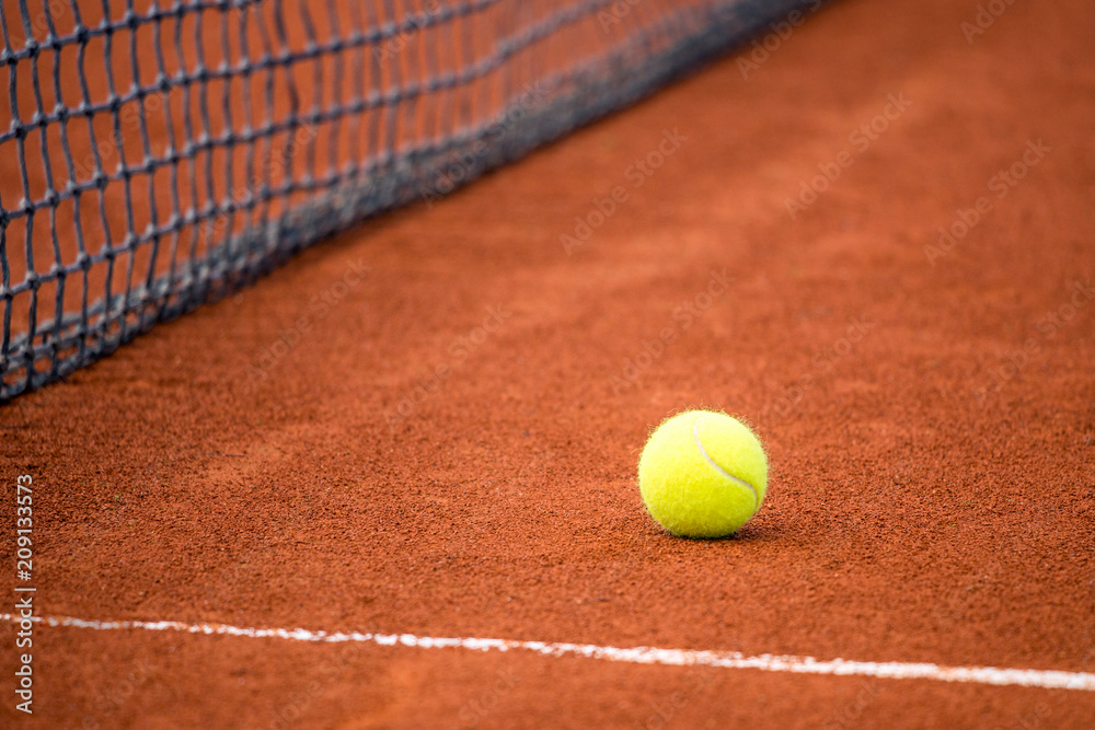Yellow ball on a clay tennis court next to the net.