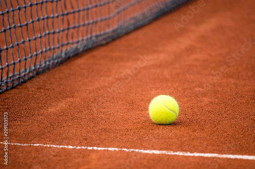 Yellow ball on a clay tennis court next to the net. © Viliam
