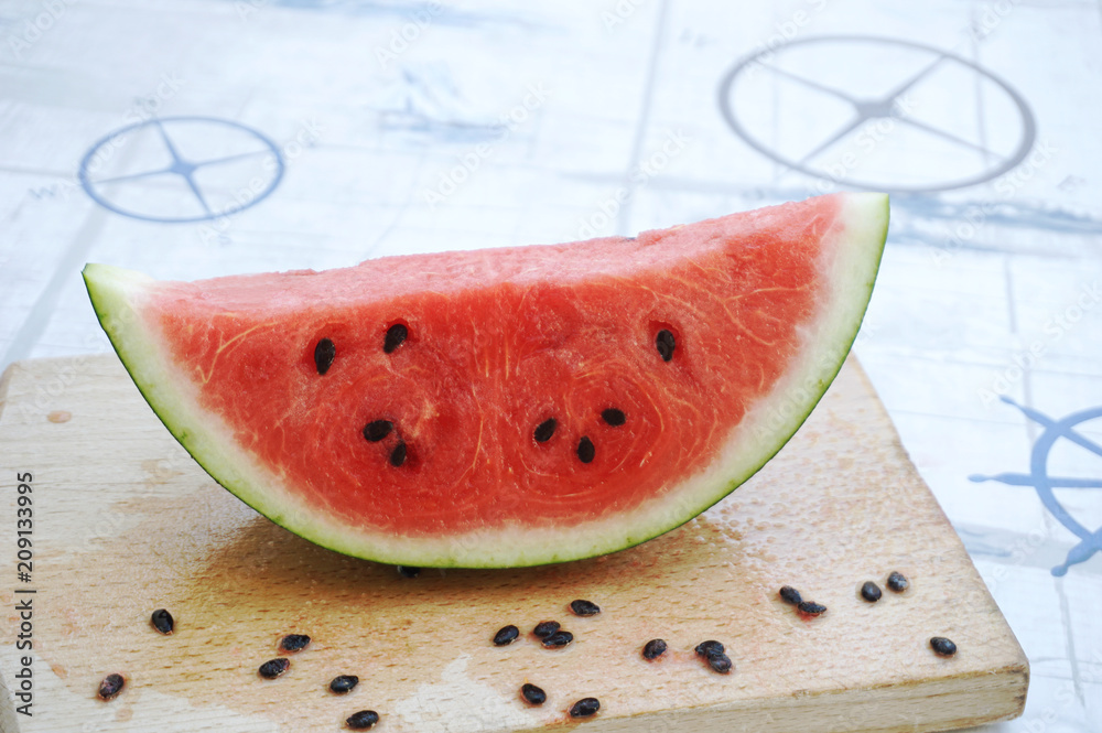 Slice of ripe watermelon on the wooden board with marine detail on tablecloth in the background Slice of ripe watermelon on the wooden board with marine detail on tablecloth in the background