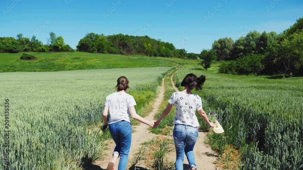 Mother and daughter holding hands running on a dirt road in the countryside holding hands. Steadicam slow motion shot. Rear view Mother and daughter holding hands running on a dirt road in the countryside holding hands. Steadicam slow motion shot. Rear view