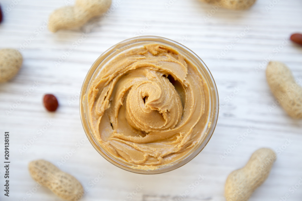 Peanut butter in a bowl and unshelled peanuts on a white wooden background, top view. Close-up. Peanut butter in a bowl and unshelled peanuts on a white wooden background, top view. Close-up.