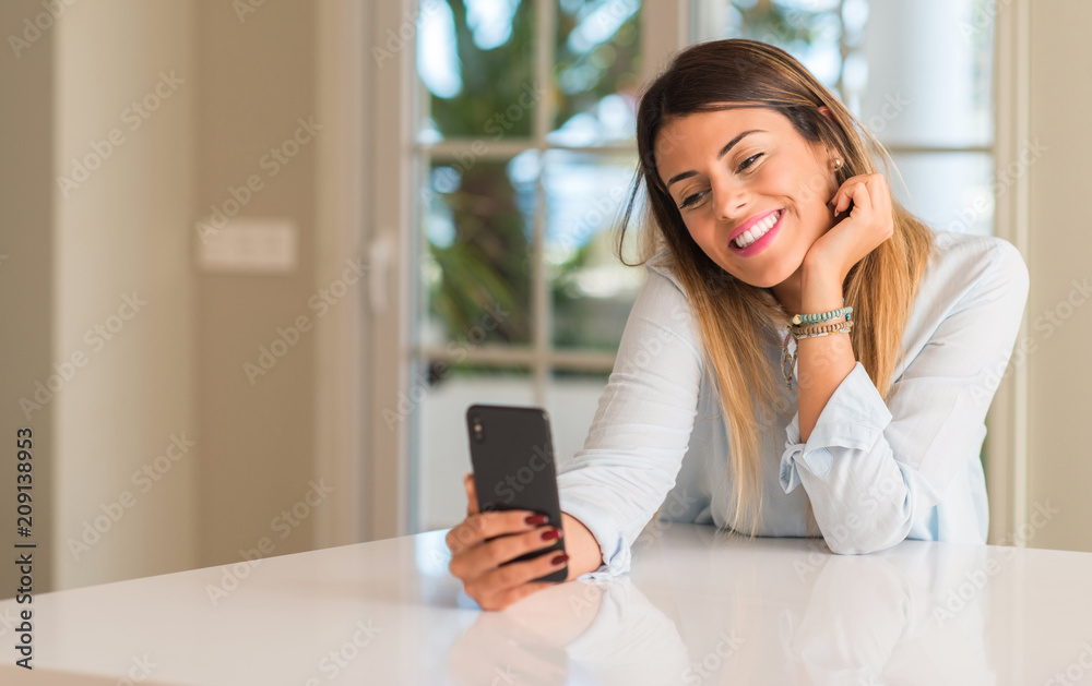Young woman smiling happy using smartphone, holding mobile phone looking at home Young woman smiling happy using smartphone, holding mobile phone looking at home
