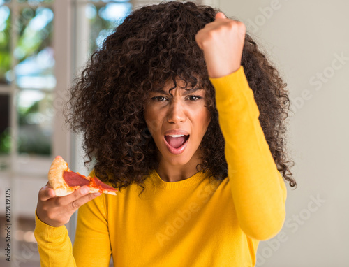 African american woman ready to eat pepperoni pizza slice annoyed and frustrated shouting with anger, crazy and yelling with raised hand, anger concept