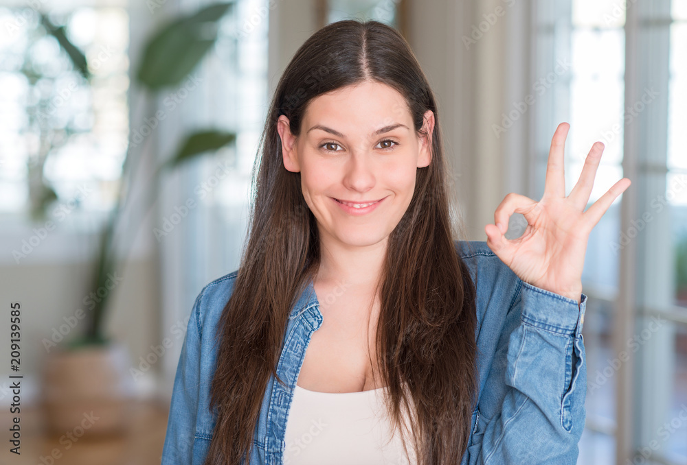 Young beautiful woman at home doing ok sign with fingers, excellent symbol Young beautiful woman at home doing ok sign with fingers, excellent symbol