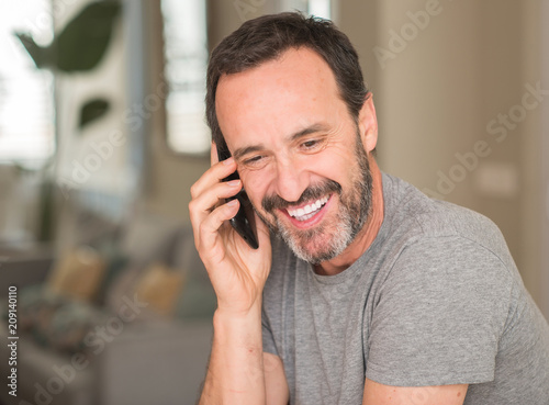 Middle age man using smartphone with a happy face standing and smiling with a confident smile showing teeth