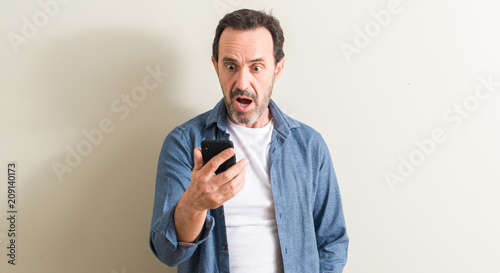 Photos Senior man using smartphone scared in shock with a surprise face, afraid and exc