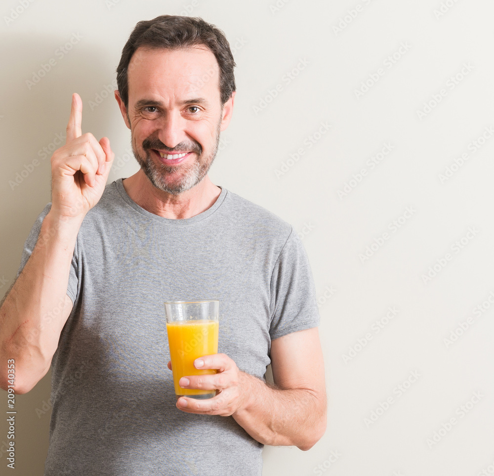Senior man drinking orange juice in a glass surprised with an idea or question pointing finger with happy face, number one Senior man drinking orange juice in a glass surprised with an idea or question pointing finger with happy face, number one