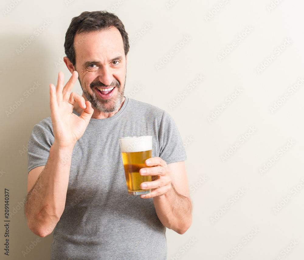 Senior man drinking beer doing ok sign with fingers, excellent symbol