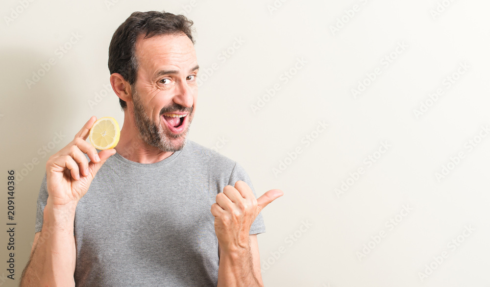 Senior man holding lemon fruit pointing with hand and finger up with happy face smiling Senior man holding lemon fruit pointing with hand and finger up with happy face smiling