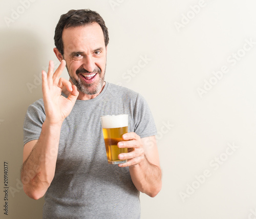 Senior man drinking beer doing ok sign with fingers, excellent symbol