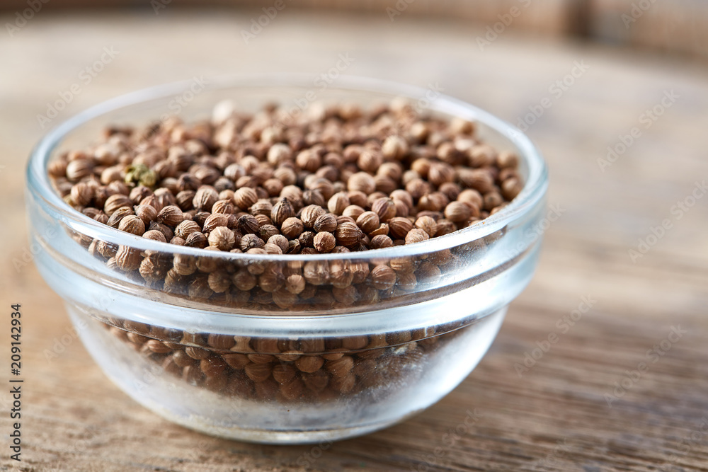 Close-up of glass bowl full of coriander seeds on rustic wooden background, top view, shallow depth of field. Close-up of glass bowl full of coriander seeds on rustic wooden background, top view, shallow depth of field.