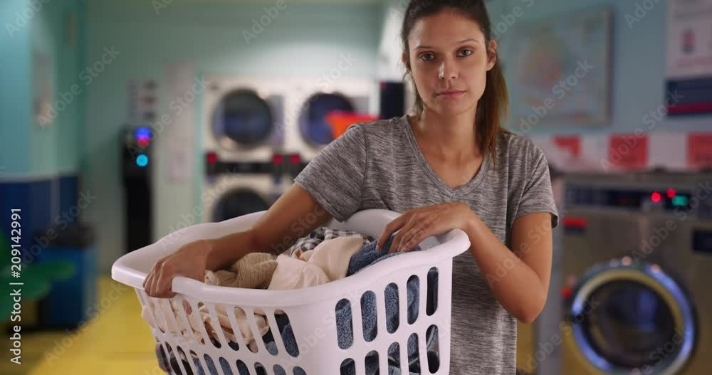 Somber young woman holding basket of clothes dirty clothes in laundry room, Casual portrait of attractive female washing and drying loads of laundry indoors, 