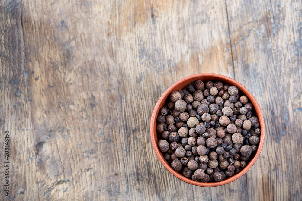 Clay bowl with dried allspice berries on vintage wooden background, top view, close-up, macro, selective focus. - obrazy, fototapety, plakaty 