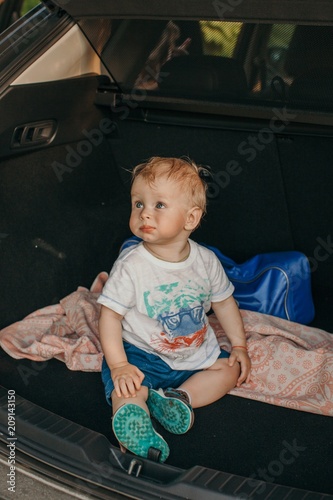 Adorable boy sitting at car trunk