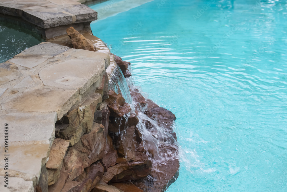 Naklejka premium Waterfall over rocks from hot tub on higher level down to swimming pool -Refreshing and cool on a summer day