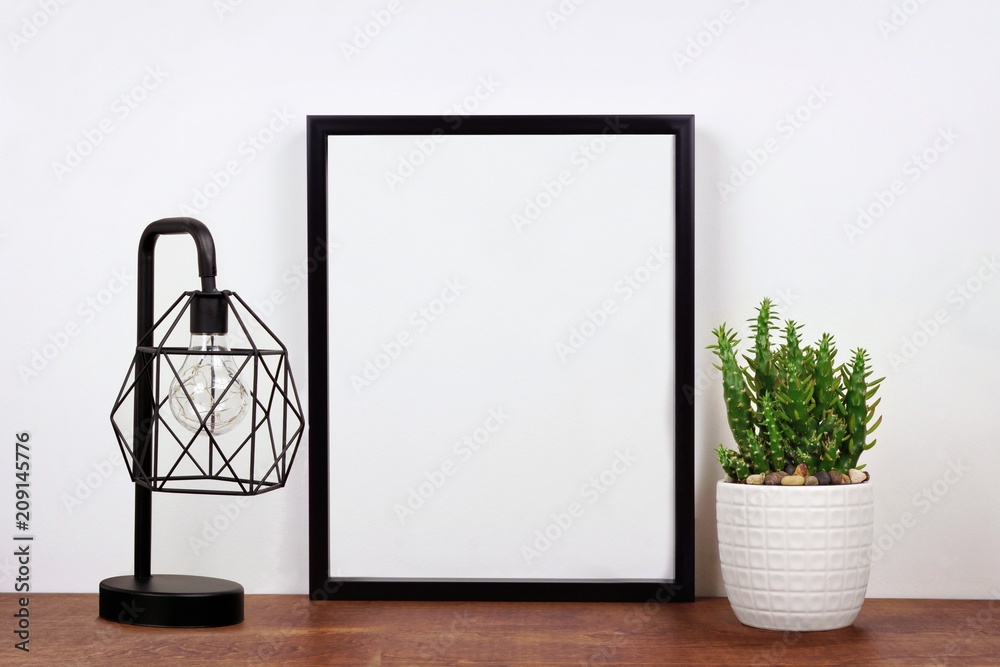Mock up black frame, cactus plant and industrial style lamp on a shelf or desk. Wood shelf and white wall. Portrait frame orientation. Mock up black frame, cactus plant and industrial style lamp on a shelf or desk. Wood shelf and white wall. Portrait frame orientation.