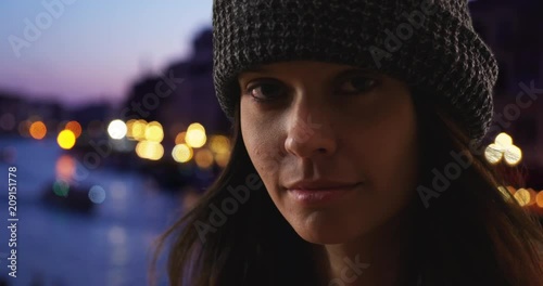 Dramatic close up portrait of woman tourist in Venice at night, Tight shot of Caucasian girl in her 20s looking at camera on vacation in Italy, 4k