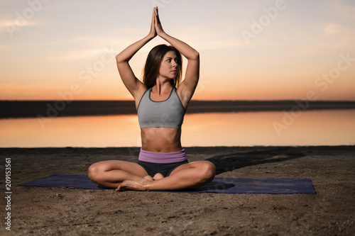woman on the beach at sunset starts doing yoga asana training . Morning natural stretch warm-up training