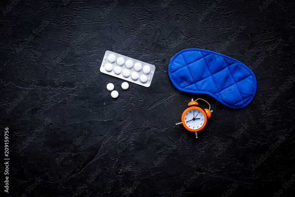 Obraz premium Medicine helps get asleep. Good sleep. Sleeping pills near sleeping mask and alarm clock on black background top view copy space