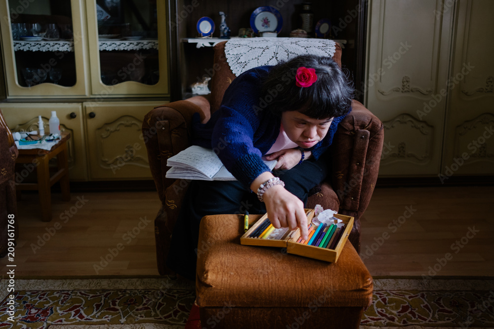 Female with down's syndrom writing at notebook with crayons Female with down's syndrom writing at notebook with crayons