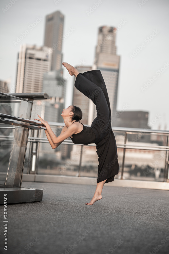Fototapeta premium Beautiful Young Girl Dancing in the City, wearing black, with background of skyscrapers