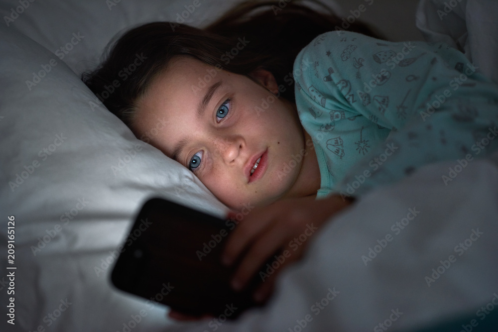 Young girl playing with phone in dark bedroom Young girl playing with phone in dark bedroom