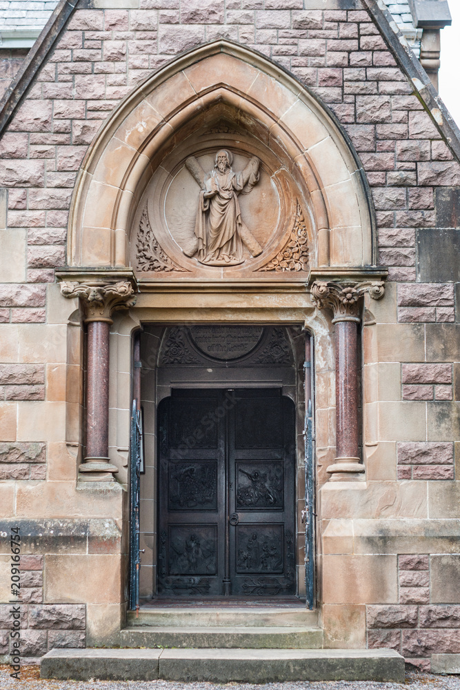 Fort William, Scotland - June 11, 2012: The main entrance into Saint Andrews Church features a heavy black relef metal door and above a stone relief image of the Saint and the cross named after him.
