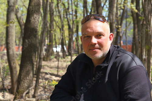 Portrait of a man 35-40 years old sitting in front of a forest in a city park.