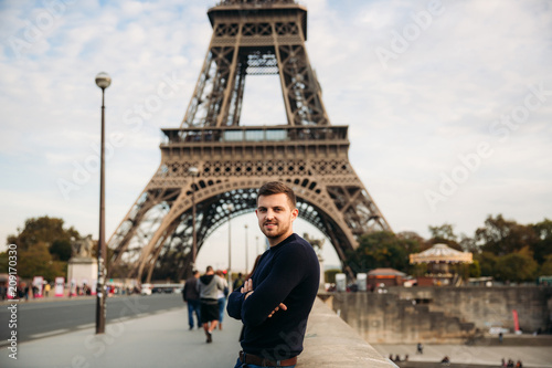 Handsome man in dark pullover is standing on the bridge background of the Eiffel Tower © Aleksandr