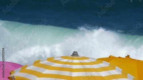 Colorful sun umbrellas on a beach, with a view of powerful waves. Slow motion close up view photo