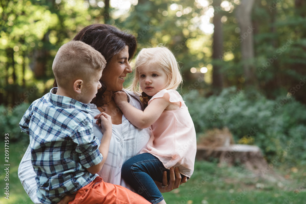 A mother holding her two children outdoors on a beautiful autumn day A mother holding her two children outdoors on a beautiful autumn day
