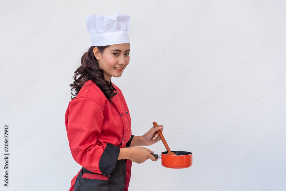Portrait of young woman wearing chef cook uniform hand holding a flying pan and wooden flipper on white background. Portrait of young woman wearing chef cook uniform hand holding a flying pan and wooden flipper on white background.