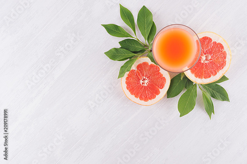 Ripe grapefruits with half slice, green leaves and juice on soft white wooden board, top view.