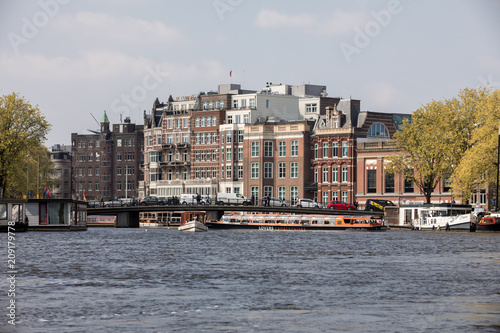  Cruise tourist boat on canal in Amsterdam, Netherlands, on a summer day. Traditional houses in the background