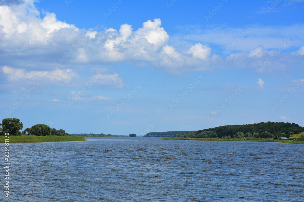 Landscape with river and forest on horizon. Cumulus clouds in sky. Russian nature. Summer day.
