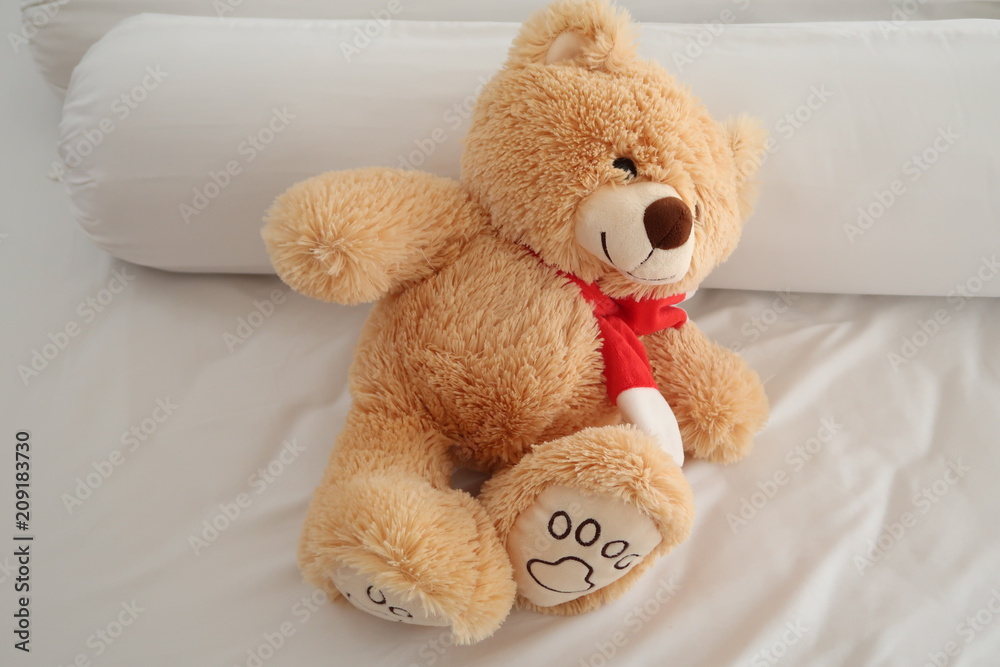 Teddy bear laying on white bed.