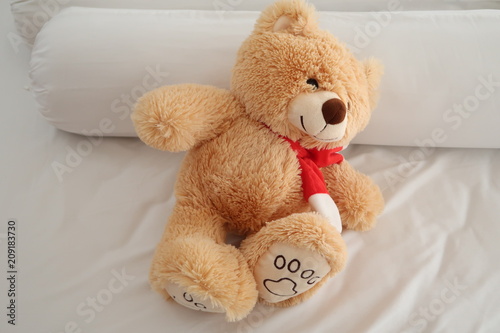 Teddy bear laying on white bed.