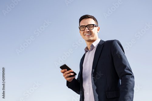 Handsome businessman. Smiling handsome businessman wearing glasses holding his smart phone in his hands